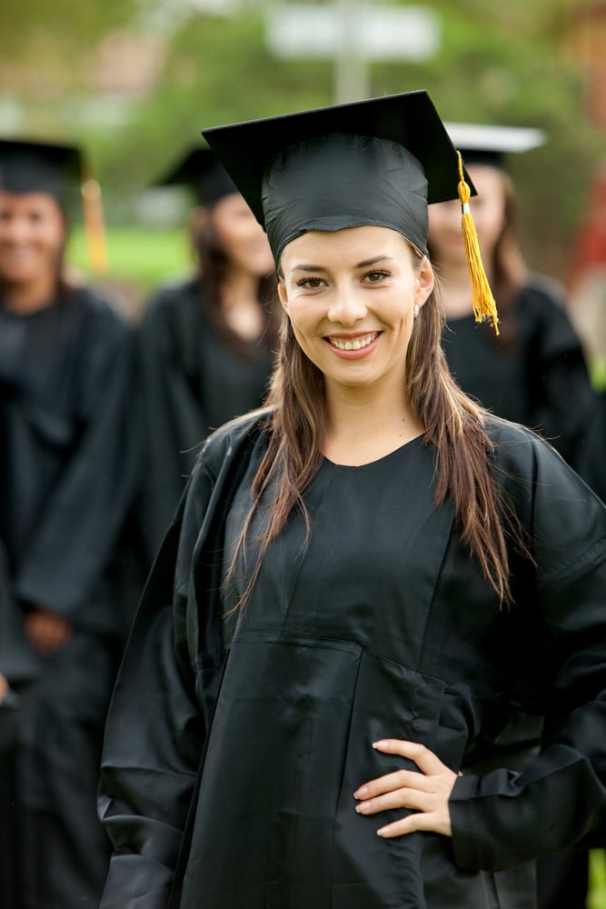 Smiling high school graduate standing outdoors with other graduates